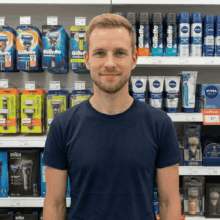 Jeroen staat voor het scheer assortiment in een winkel, in de achtergrond zie je gillette en oneblade scheermesjes, maar ook baard verzoring producten.